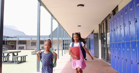 Two Girls with Backpacks Walking in School Hallway
