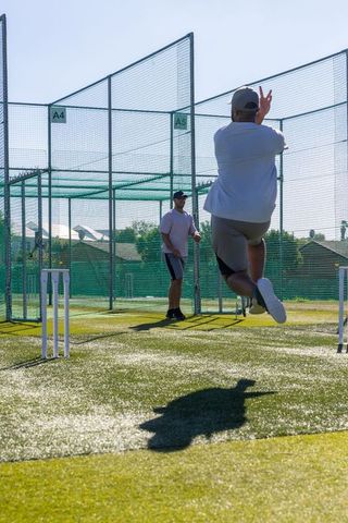 Amateur cricket bowling practice in sunlit outdoor nets on artificial turf with wickets