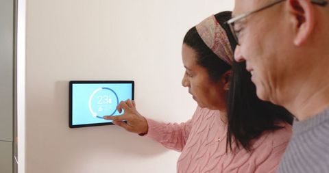 Senior couple adjusting smart thermostat for home comfort