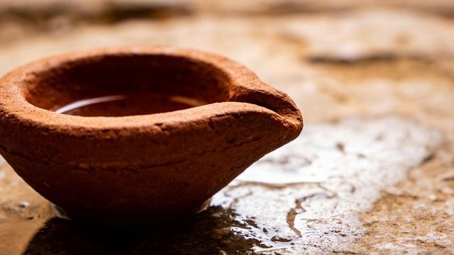 Unlit clay diya resting on wet stone with oil puddles and warm terracotta texture