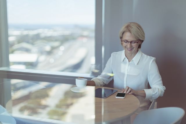 Smiling businesswoman using smart phone while sitting at table in office