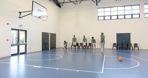 Diverse Basketball Team Training with Coach Using Smartphone in Gymnasium