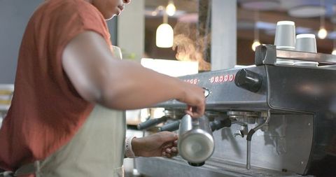 African american barista steaming milk using commercial espresso machine for latte art