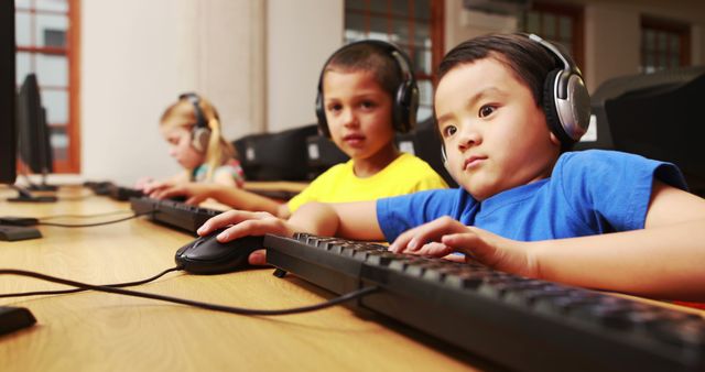 Young children in a classroom setting are using desktop computers while wearing headphones. They are focused on their tasks, which likely involve educational software or activities. This image can be used for educational materials, school promotional content, and articles on modern digital learning and technology use in education.