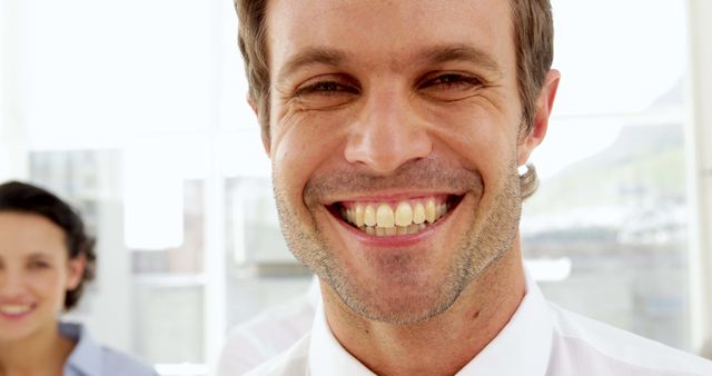 Close-up of a young smiling man in an office setting. Perfect for depicting concepts of workplace happiness, professional success, and positive work environments. Ideal for use in business promotions, company websites, and employee engagement materials.