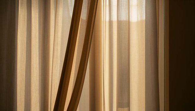 Sunlit sheer beige curtains filtering warm morning light through pleated drapery