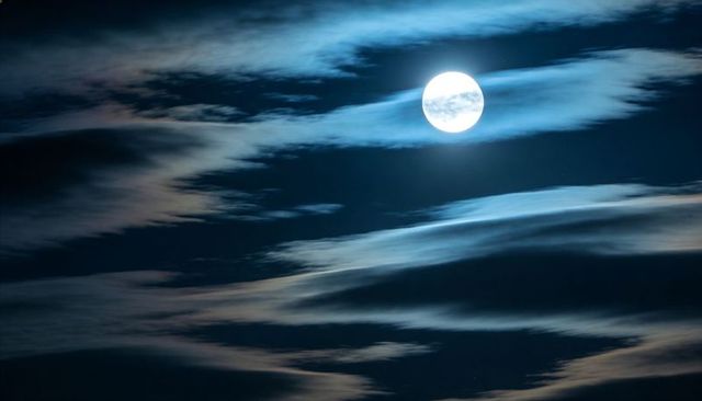Glowing full moon illuminating wispy cirrus clouds across deep blue night sky with soft halo