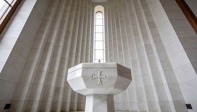 Octagonal marble baptismal font standing in minimalist chapel with tall clerestory window