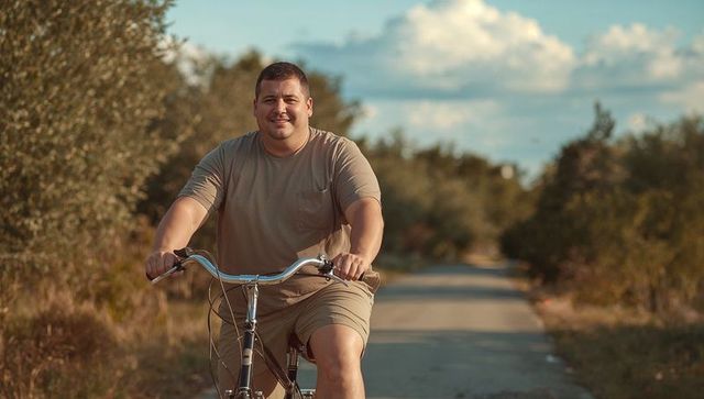 Riding smiling man cycling along sunlit rural lane in beige outfit at golden hour