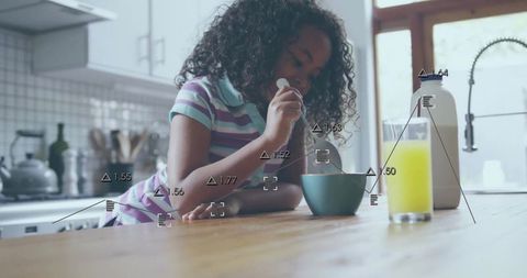 Curly girl stirring breakfast cereal on wooden countertop in modern sunlit kitchen morning routine