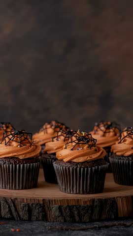 Vertical video showing Halloween cupcakes with orange frosting and spiderweb chocolate on wood slab