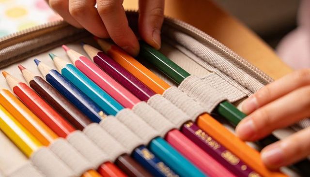 Student hands organizing colored pencils in zippered fabric case for school art projects