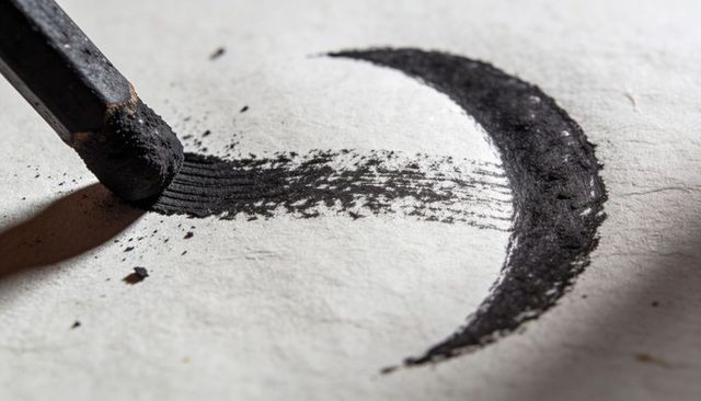 Compressed charcoal stick creating dense crescent stroke on textured paper macro closeup