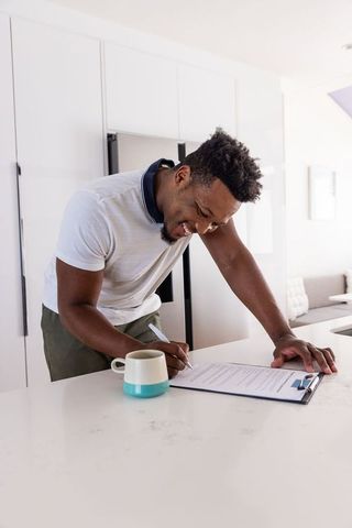 African american man signing documents on modern minimalist kitchen island with coffee