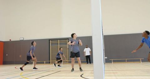 Diverse male team playing indoor volleyball in school gym during competitive training session