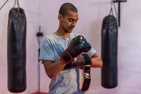 Asian man fastening boxing gloves in industrial gym with heavy bags for training