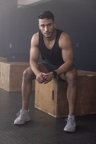 Muscular male athlete resting on plyometric box catching breath after intense workout