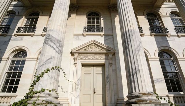 Sunlit neoclassical marble facade with fluted columns and decorative pediment entrance