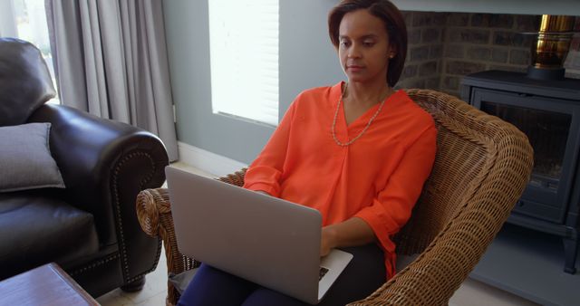 Front view of black woman working on laptop in living room at home. Black woman sitting on armchair at home 4k