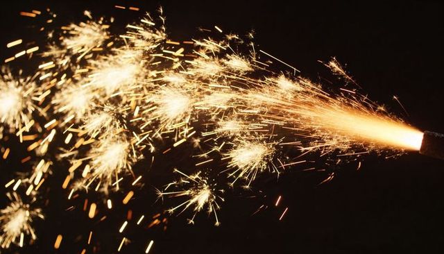 Handheld sparkler throwing golden sparks at night, glowing ember burst and streaks