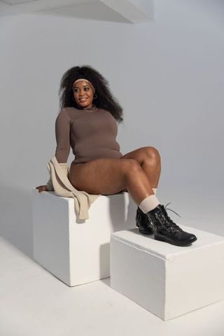 African american model posing on white blocks wearing brown bodysuit and black boots