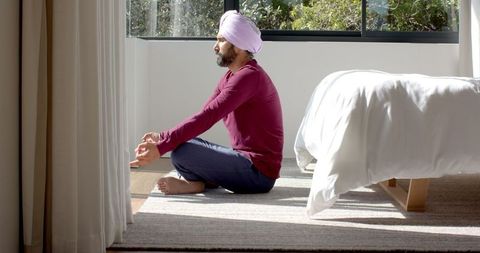 Man in turban meditating on floor at home with sunlit ambiance