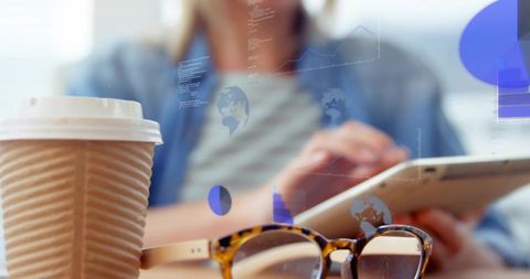 Freelancer tapping tablet with coffee and tortoiseshell glasses, analytics overlay