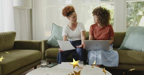 Two women collaborating over laptop and documents on cozy living room sofa