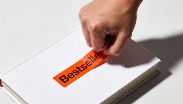 Hand peeling bright orange bestseller sticker from white hardcover book