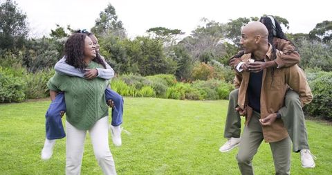 Parents Carrying Children Piggyback in Park Laughing and Playing Together