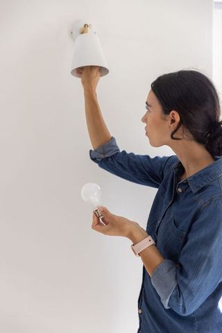 Woman replacing wall sconce bulb in minimal hallway | diy home lighting renovation