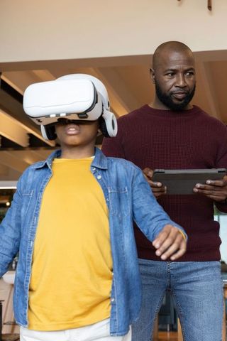 African American Father Supervising Child Using VR Headset While Controlling Tablet