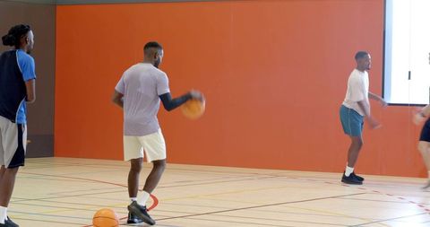 Male basketball players dribbling on multipurpose indoor court during team training drill