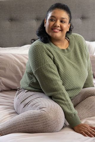 Asian middle-aged woman relaxing on bed wearing green knit sweater and ribbed loungewear