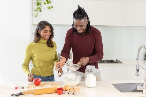 Multicultural couple baking at modern kitchen island, sifting flour and mixing batter