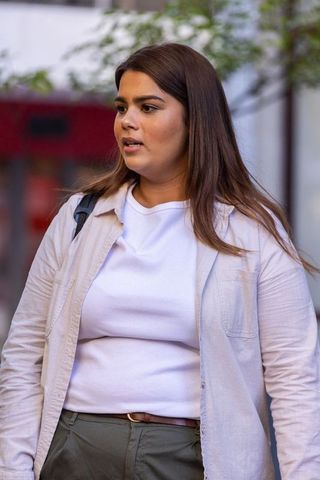 African american woman standing and talking on urban street wearing beige shirt, backpack