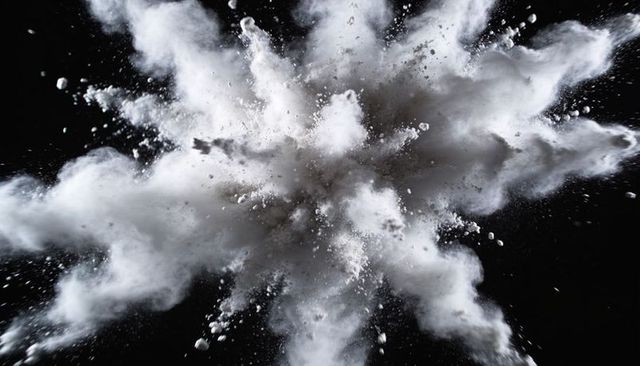 High-speed white powder explosion creating plume of particles and dust on black background