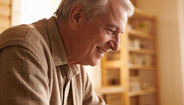 Senior man smiling and leaning in cozy sunlit home, wooden shelves and warm mood