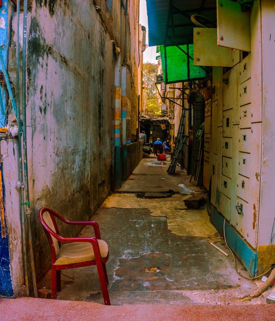Narrow alleyway with colorful plastic chair, urban living - Download Free Stock Photos Pikwizard.com