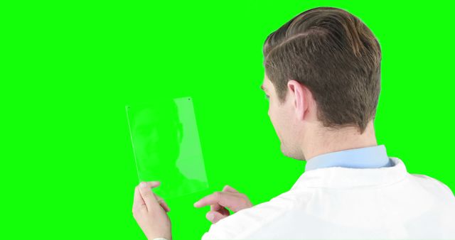 A Caucasian man in professional attire examines a transparent green screen tablet, with copy space. His focused attention suggests he might be a businessman or a tech professional analyzing data or a digital concept.