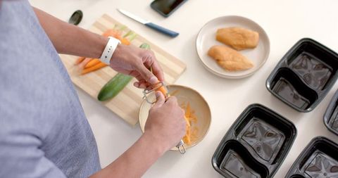African american man meal prepping peeling carrots with chicken and black meal containers