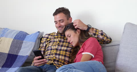 Couple Relaxing at Home, Man Using Smart Phone, Woman Resting on Shoulder