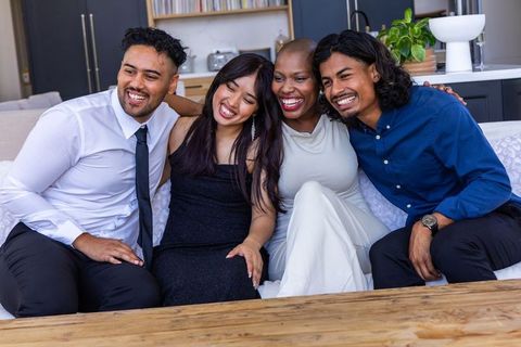 Diverse friends laughing and sitting together on sofa in modern open-plan living space