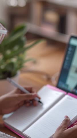 Vertical video of woman taking notes during online meeting at minimalist home workspace