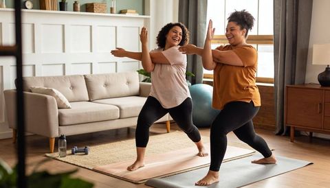 Two women practicing partner yoga and stretching in cozy living room workout