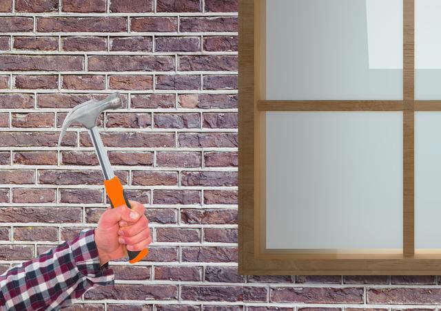 Hand holding hammer in front of brick house wall, ideal for illustrating concepts related to construction, DIY projects, home improvement, and renovation. Useful for blogs, articles, advertisements, and instructional materials on building and repair work.