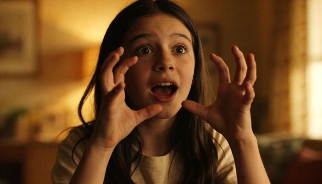 Preteen girl expressing surprise with playful claw gesture in warm cozy living room
