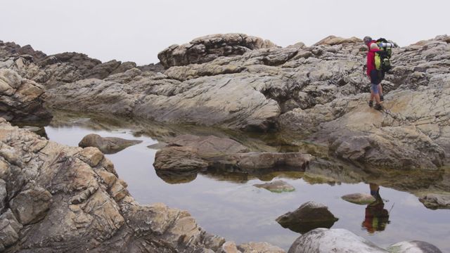 A senior couple explores a rocky landscape, equipped with backpacks and Nordic walking poles. Their accessories are indicative of a healthy, adventurous lifestyle, ideal for conveying concepts of active aging and outdoor leisure. This scene suits use in advertisements promoting fitness and well-being for older adults, travel content targeting the senior demographic, or health insurance visuals portraying wellness and vitality.