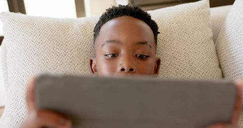 African American Boy Reclining on Couch Using Tablet Closeup Warm Sunlit Interior