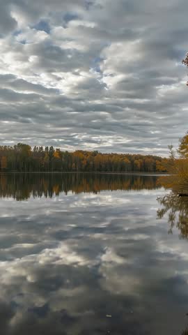 Vertical video capturing moody autumn lake reflection under dramatic cloudy sky and gentle ripples